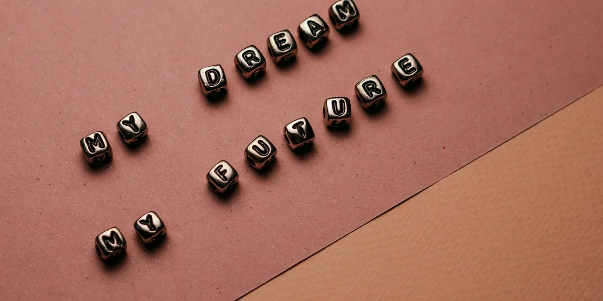Beads with black blocks and white letters spelling 'I DREAM MY DREAM' scattered on a pink background.