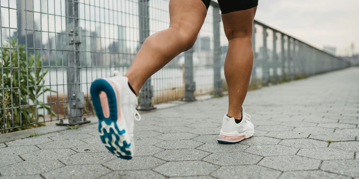 Person running along a paved walkway next to a metal fence, wearing white and blue sneakers, illustrating the act of fleeing in a chase dream.