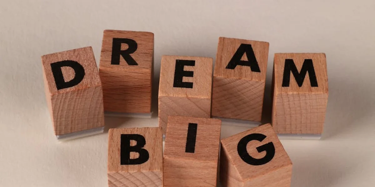 Wooden blocks arranged to spell the words 'DREAM BIG' on a light beige surface.