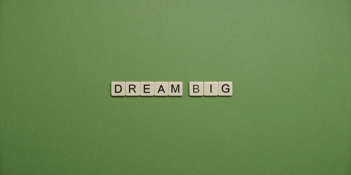 Green background with Scrabble-style letter tiles spelling 'DREAM BIG' centered
