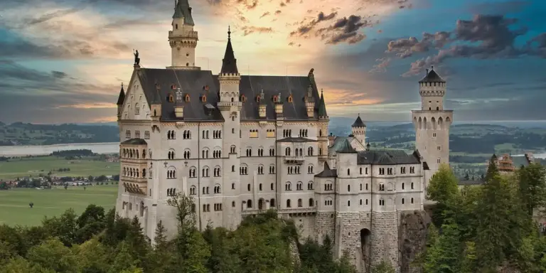 A grand medieval castle with multiple towers atop a forested hill, under a dramatic sky.