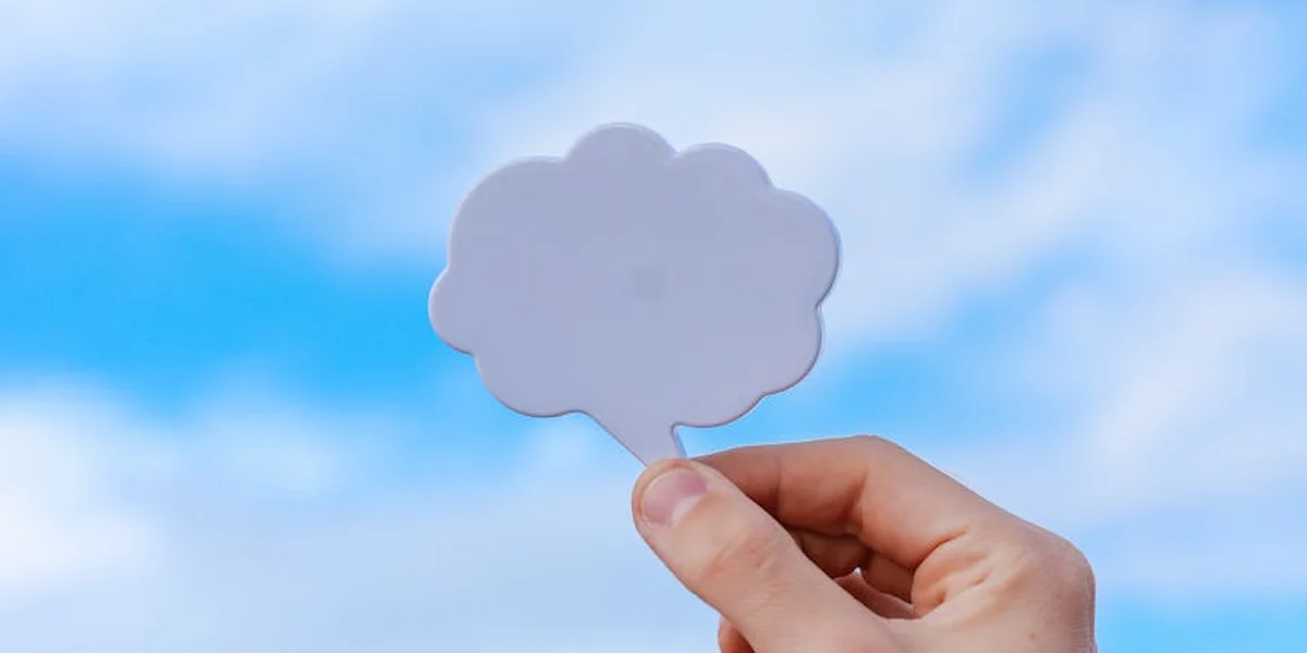 Hand holding a cloud-shaped cutout against a blue sky, symbolizing blending general dream dictionaries with personal dream wisdom.