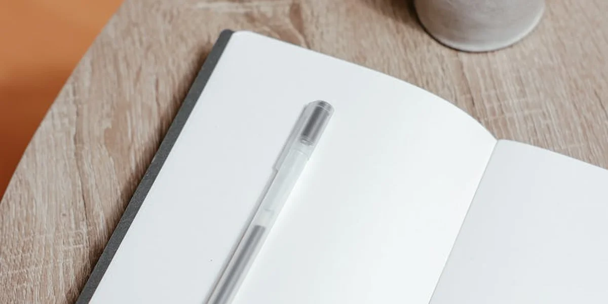 Close-up of a silver pen resting on an open white notebook on a wooden desk.