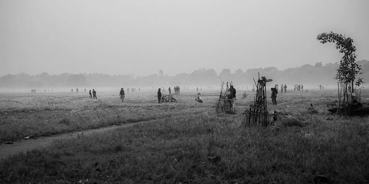 Black-and-white photo of an open, misty field with distant figures and sparse trees, conveying a sense of pursuit and escape.