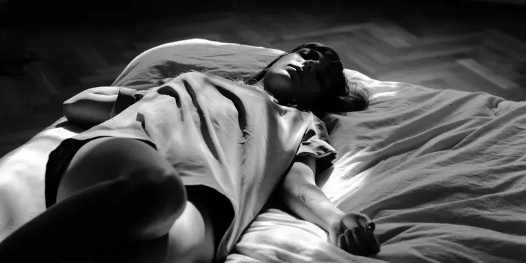 A person lies on a bed in black and white, eyes closed, suggesting sleep or a dream-like state.