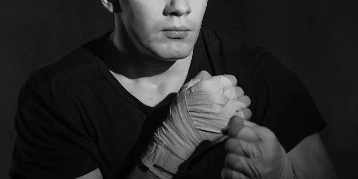 Close-up of a person wearing boxing gloves, fists clenched in front of their chest in grayscale