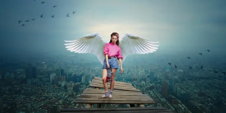 A person wearing a pink top and denim shorts with large white wings stands on a weathered wooden platform high above a city skyline, with birds in the sky.
