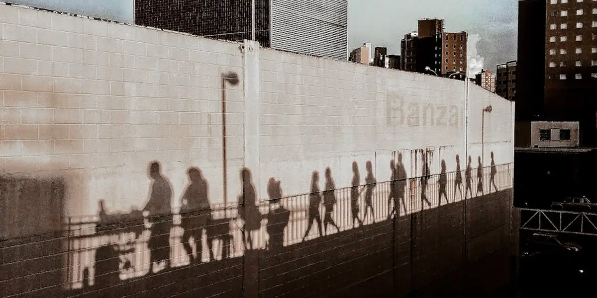 Silhouetted figures walking along a tall wall, their long shadows stretched across the surface.