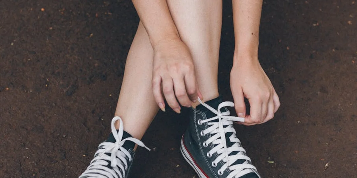 Close-up of hands tying white sneakers on a dark dirt surface