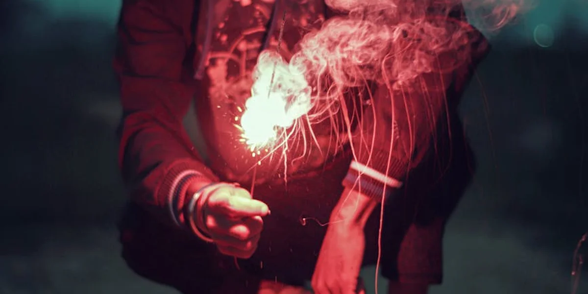 Close-up of a person in a red shirt holding a bright sparkler, with glowing sparks and smoky wisps