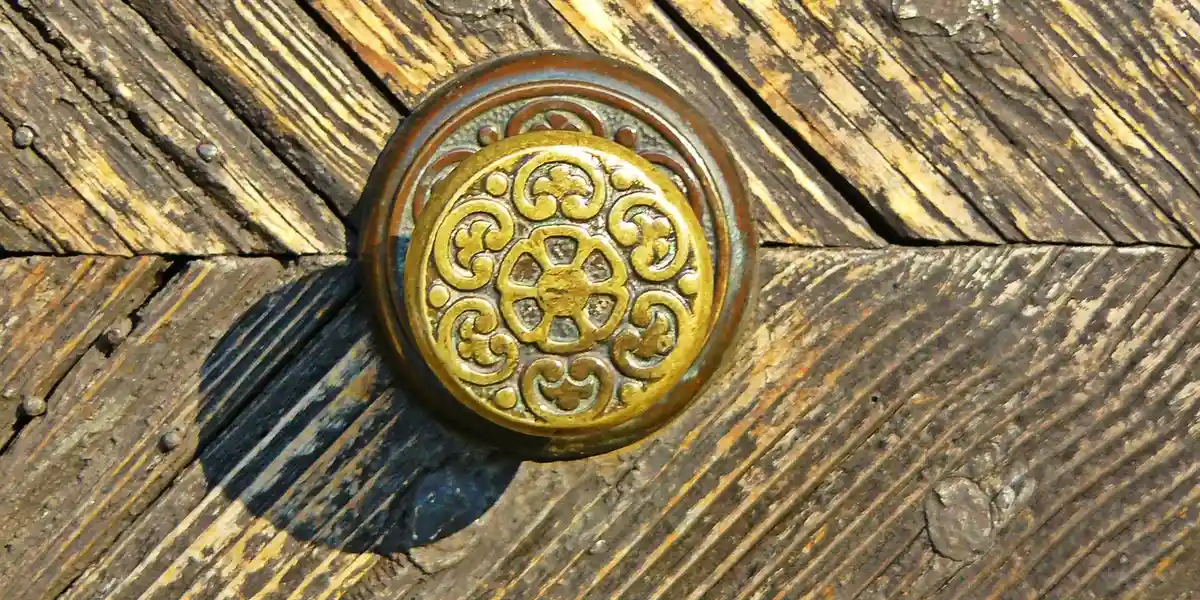 Close-up of an ornate brass door knob on a weathered wooden door