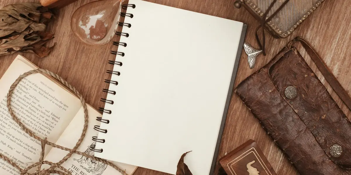 A blank notebook lies open on a wooden desk beside a dream journal, with a leather-bound notebook, a string of beads, and a glass ornament - creating a calm setup for recording dreams.