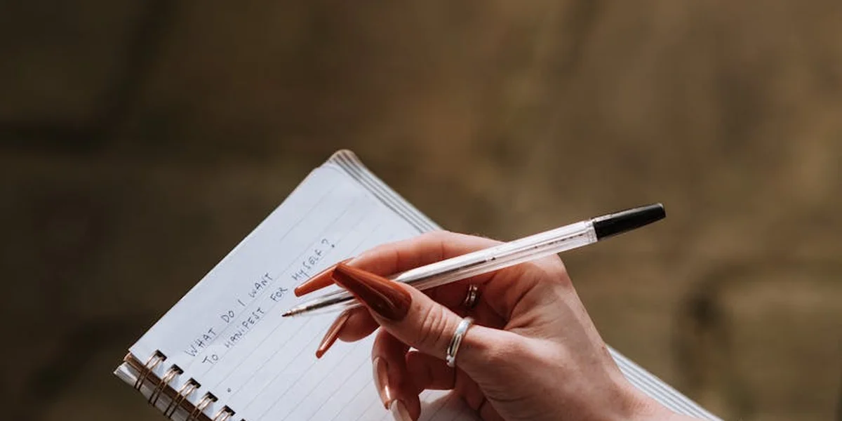 Close-up of a hand holding a white pen over an open spiral notebook, ready to write dreams as part of a spiritual practice
