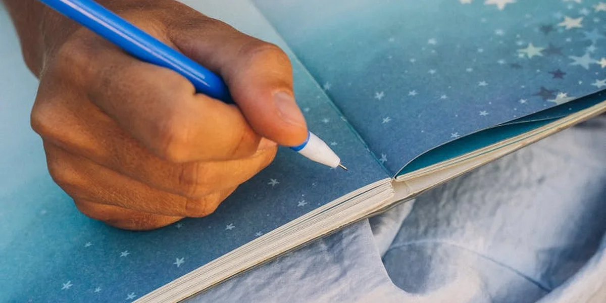 Close-up of a hand writing in a dream journal with a blue pencil on a blue star-patterned page