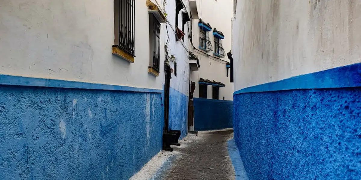Narrow alley with white walls and blue lower walls, suggesting a labyrinth-like passage.