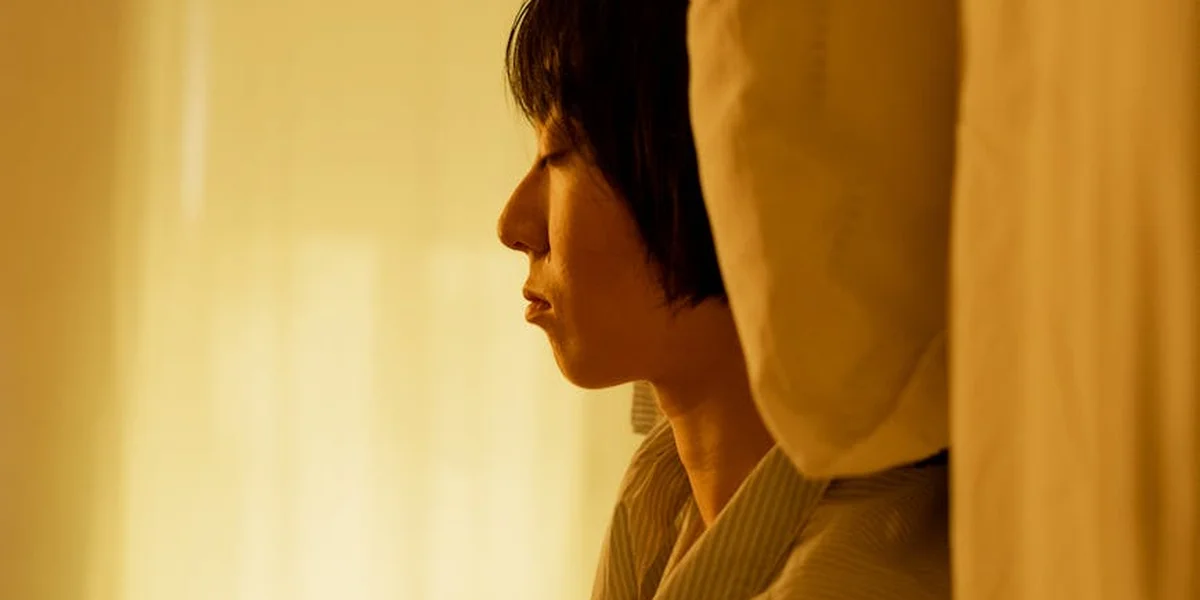 Profile of a person with short dark hair wearing a light hoodie, facing left in warm amber light.