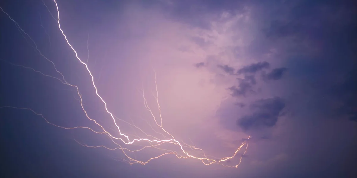 Dramatic night sky with bright white lightning forks weaving through purple-tinged clouds, illustrating color symbolism in dream imagery.