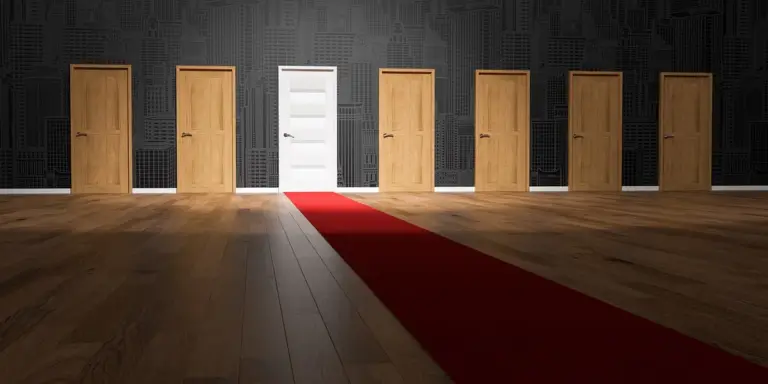 A dim hallway with several wooden doors along a black wall; a bright white door in the center, with a red carpet leading toward it.