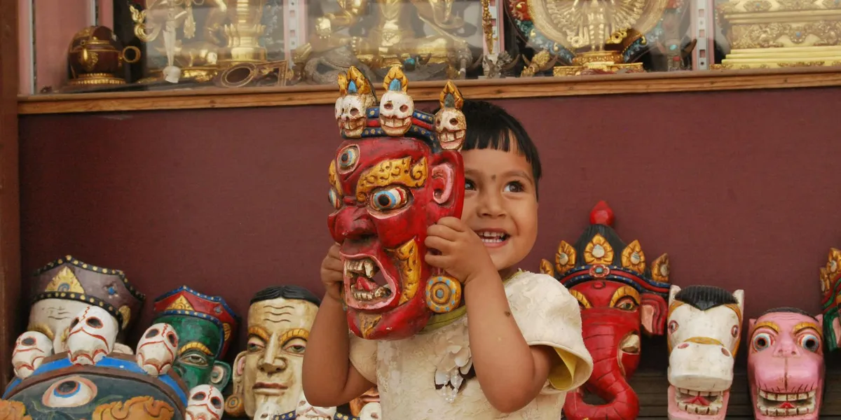 A child holding a red, fierce-looking mask while colorful masks line the background.