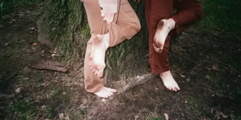 Two people standing barefoot outdoors near a tree, showing their feet.