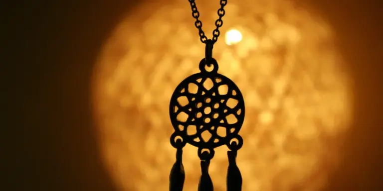 Ornate circular geometric pendant hanging on a chain, illuminated by a warm golden glow.