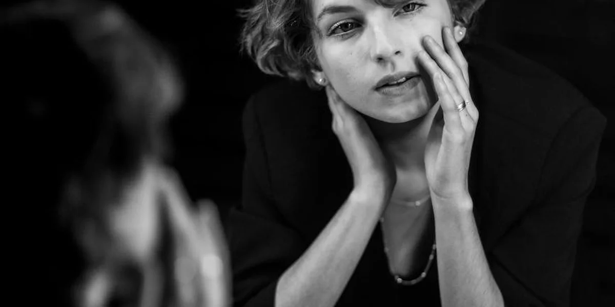 Black-and-white photo of a thoughtful woman with hands resting on her cheeks, looking off to the side.