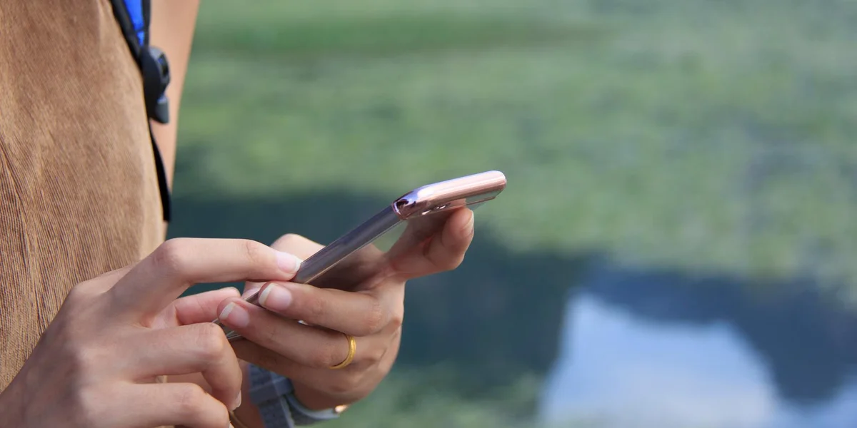 Close-up of a person holding a smartphone outdoors, fingers poised over the screen.