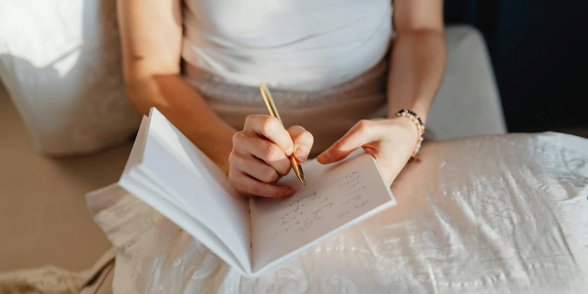 Close-up of a person writing in a notebook on a bed, illustrating dream journaling to improve recall.