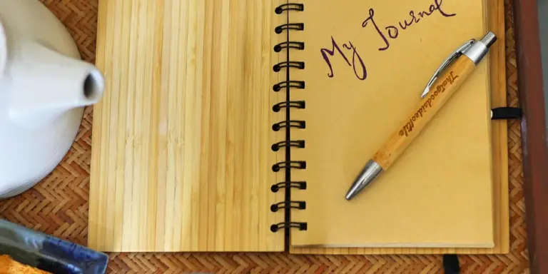 Open notebook titled 'My Journal' with a wooden desk and a pen, plus a teapot nearby.