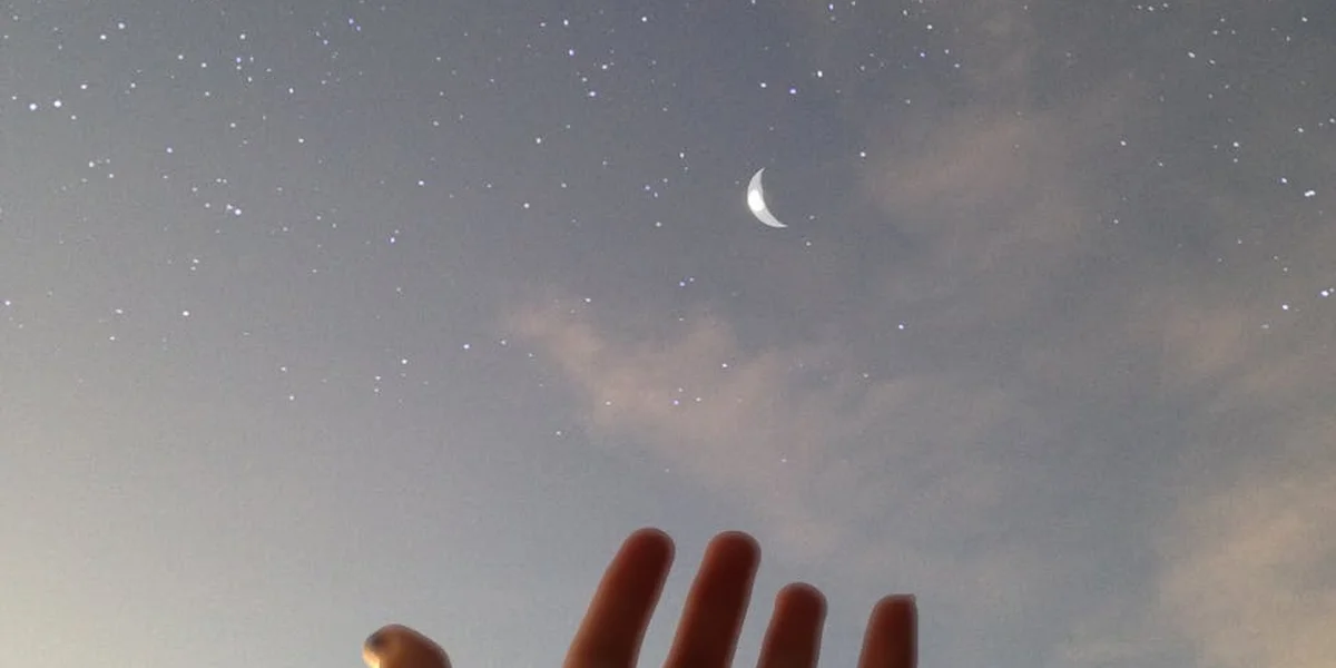 Hands reaching toward a crescent moon and a star-filled night sky with soft clouds.