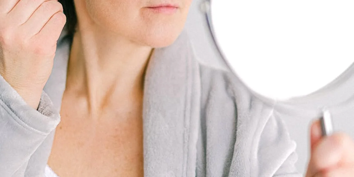 Close-up of a person in a soft robe looking into a mirror while touching their temple, conveying reflection and vulnerability.