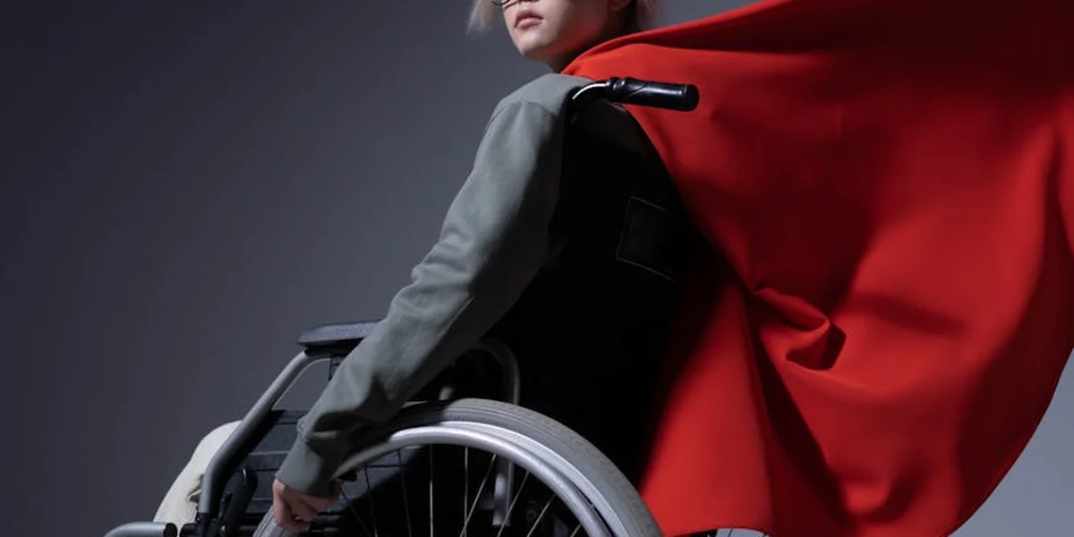 Person in a wheelchair wearing a red cape like a superhero against a dark backdrop.