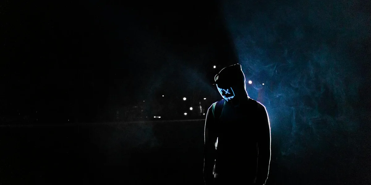 Silhouette of a person standing in darkness, backlit by blue light, symbolizing vulnerability, authenticity, and the shedding of social masks.
