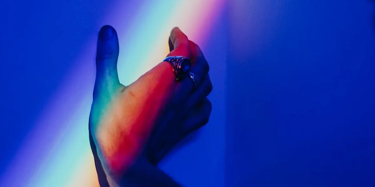A close-up of a hand under blue and magenta lighting, wearing a ring, with a dreamlike ambiance suggesting symbolic meaning.