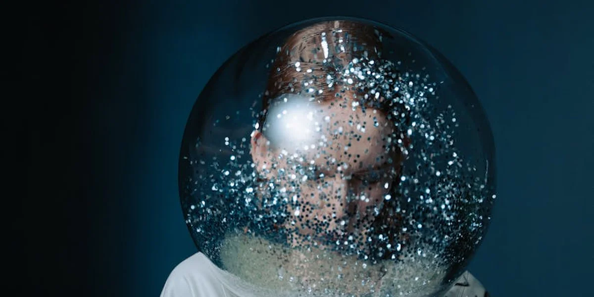 A glass sphere containing a blurred human face, with sparkling specks and a dark blue background.