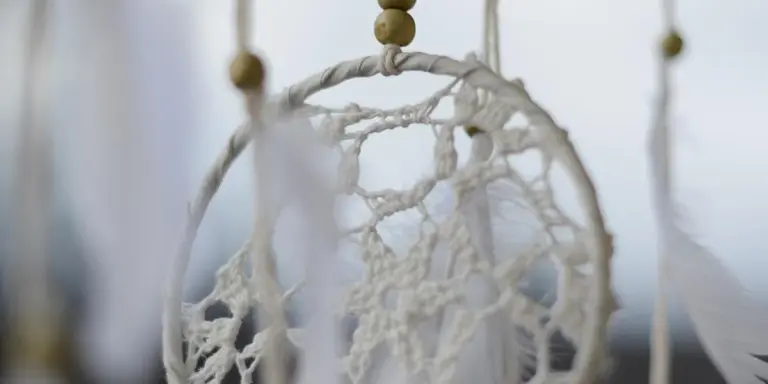 Close-up of a white dreamcatcher with intricate netting and beads, blurred background