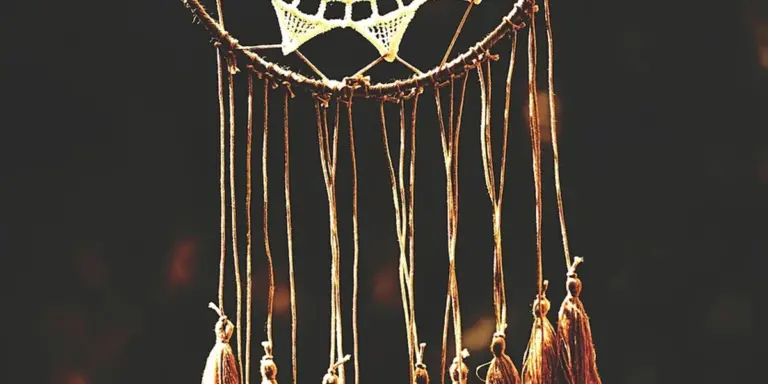 Close-up of a dreamcatcher with hanging threads and beads against a dark background