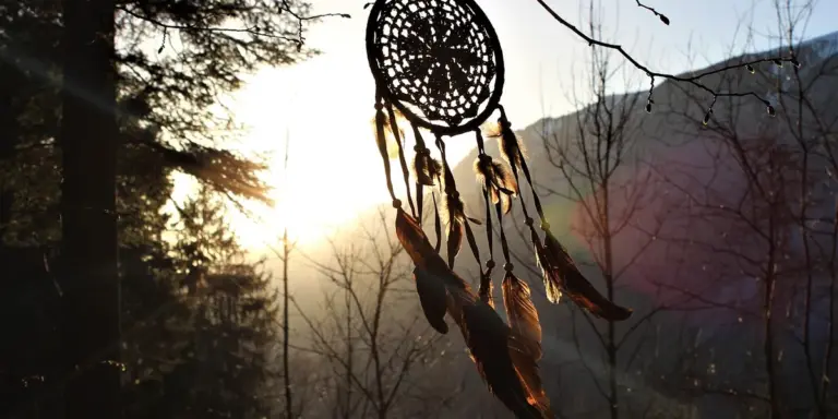 Dreamcatcher hanging among trees with sun rays at dawn over a forested valley.