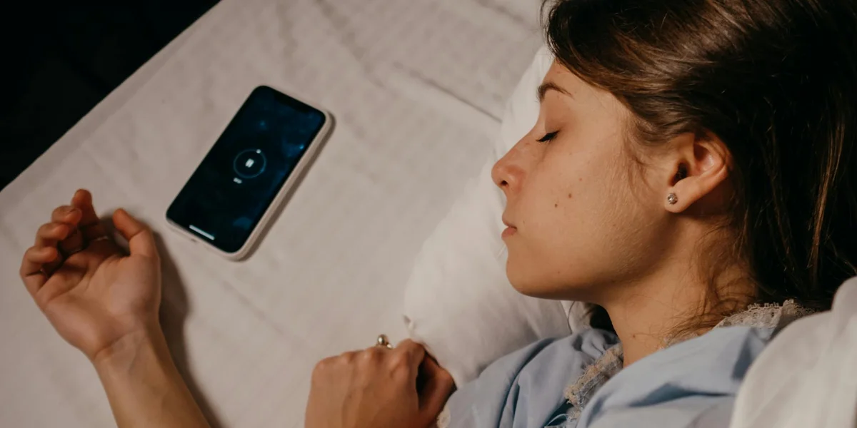 A person sleeping in bed with a smartphone resting nearby