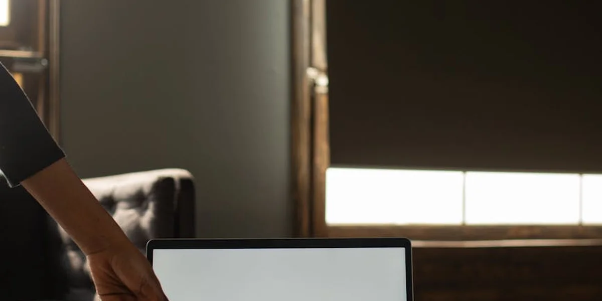 Dimly lit workspace with a hand reaching toward a laptop on a desk, conveying time pressure and introspection.