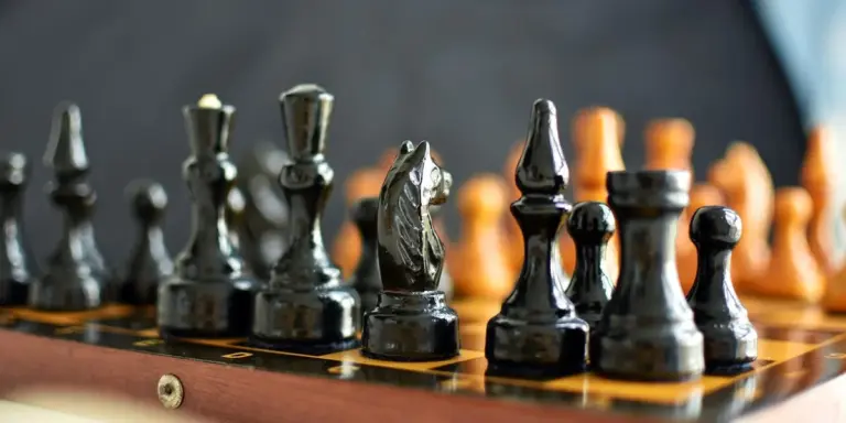 Close-up of black chess pieces on a board with orange pieces blurred in the background.
