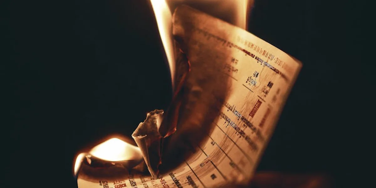A sheet of paper on fire against a dark background, flames licking the edges.