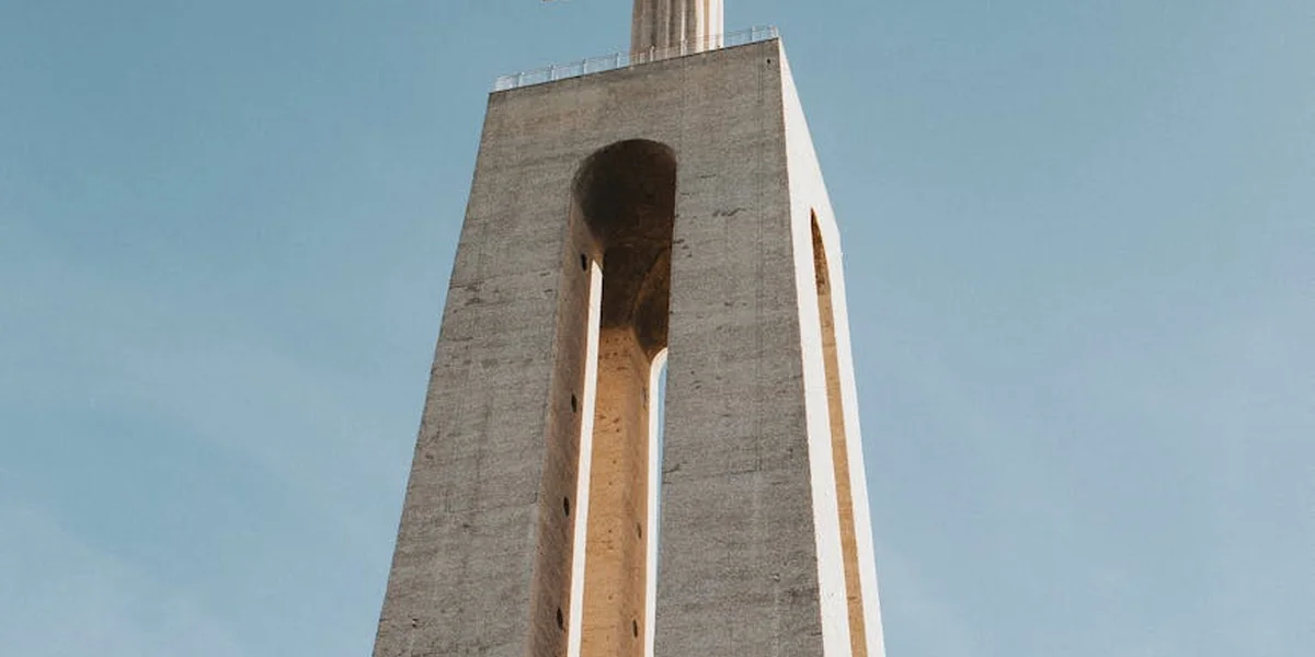 Concrete church tower with arched openings rising against a clear blue sky.