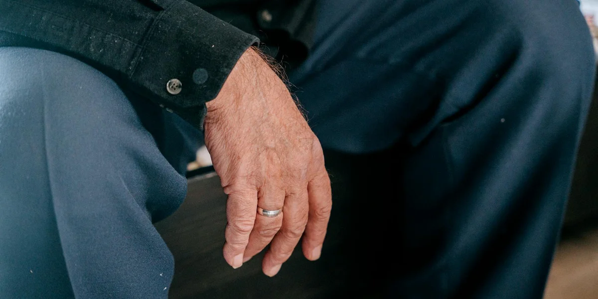 Close-up of a hand with a wedding ring resting on the knee.
