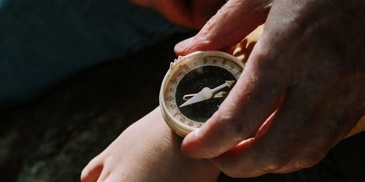 Close-up of a hand holding a compass against a dark, blurred backdrop, symbolizing inner guidance