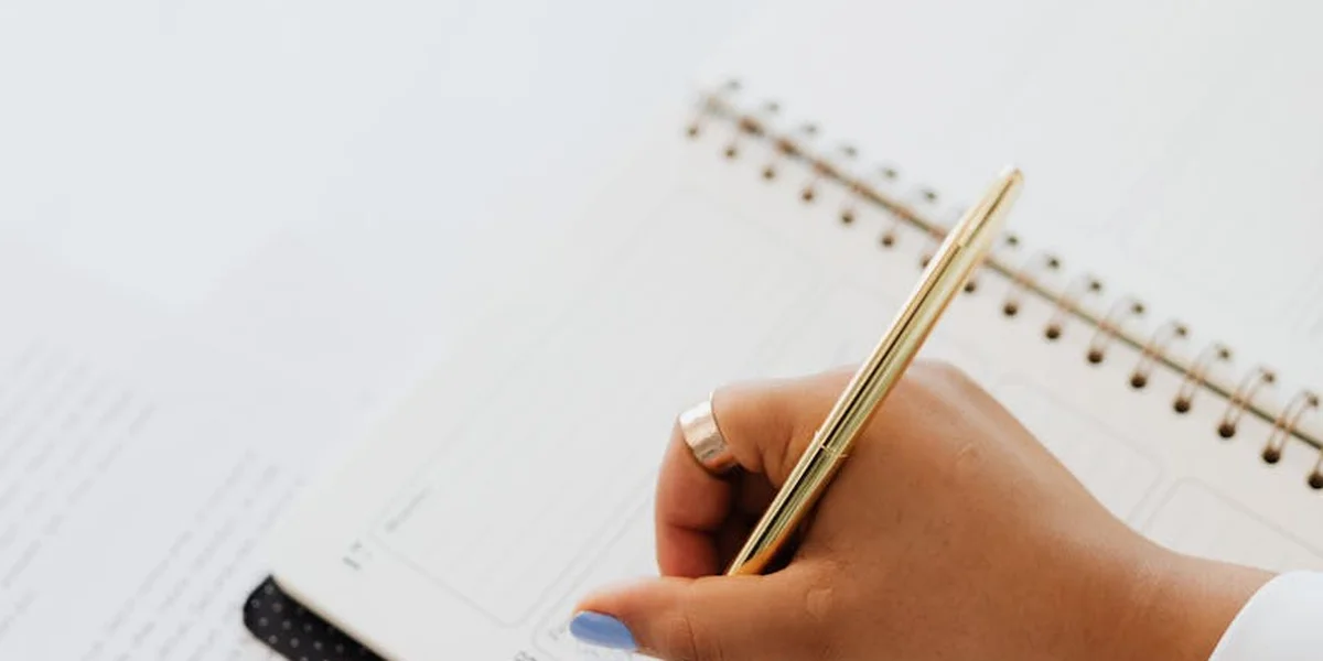 Close-up of a hand holding a gold pen over an open spiral notebook, ready to write