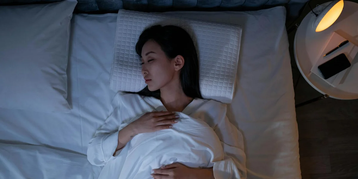 A person resting in a bed with white pillows in a softly lit bedroom