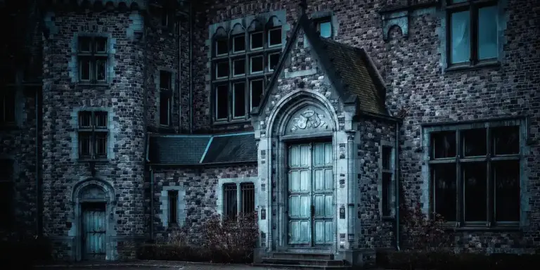 Dark, weathered brick building with a gothic arched doorway and tall, shadowed windows, set under a gray sky.