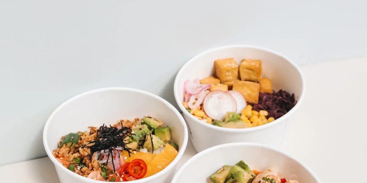 Three bowls of food with corn kernels and colorful toppings on a light surface.