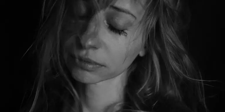 Black-and-white portrait of a woman with her eyes closed, suggesting sadness or emotional introspection.